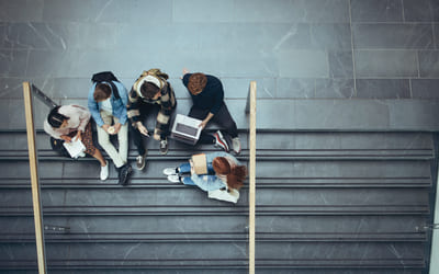 Fem elever sitter i en grå steintrapp. Bilde.