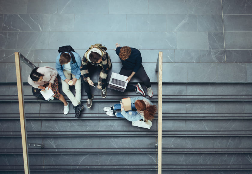 Fem elever sitter i en grå steintrapp. Bilde.
