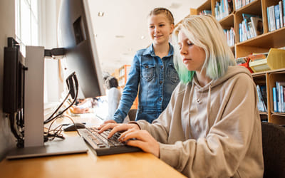To elever sitter foran en dataskjerm på et bibliotek. Bilde.