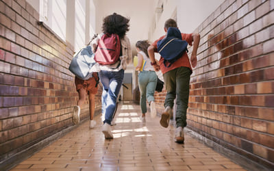 Fire elever løper i en gang på en skole. Bilde.