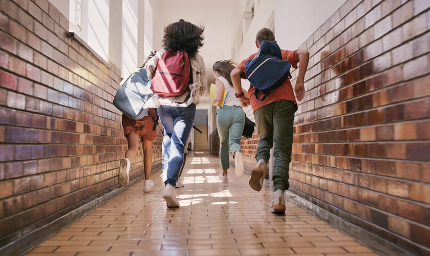 Fire elever løper i en gang på en skole. Bilde.