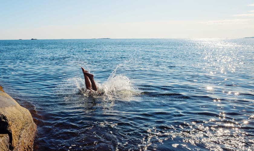 Person som stuper ut i sjøen i fint vær. Bilde.