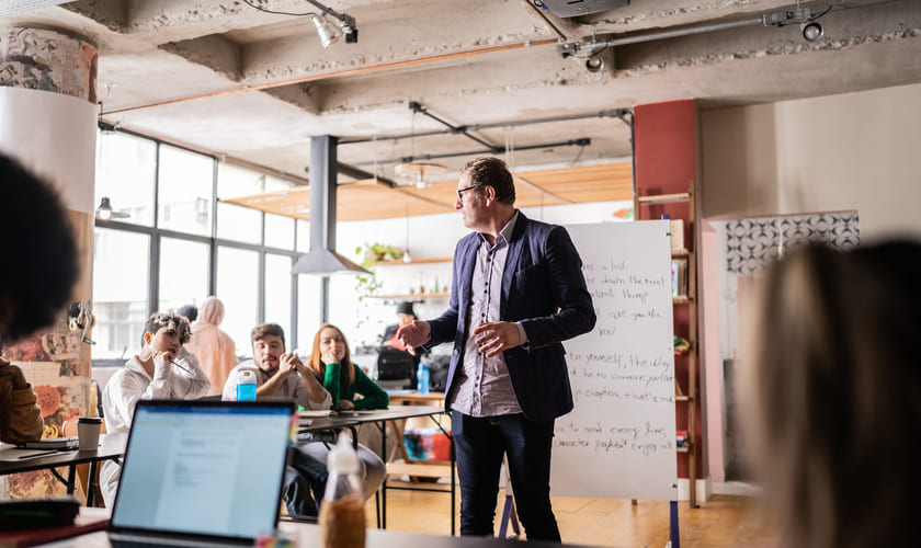 En lærer står ved en flipover foran elever og underviser. Bilde.