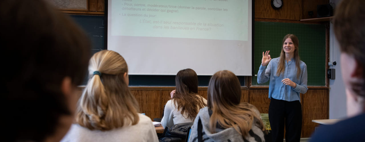 En lektor står foran en klasse med oppgaver i fransk på en prosjektor. Bilde.