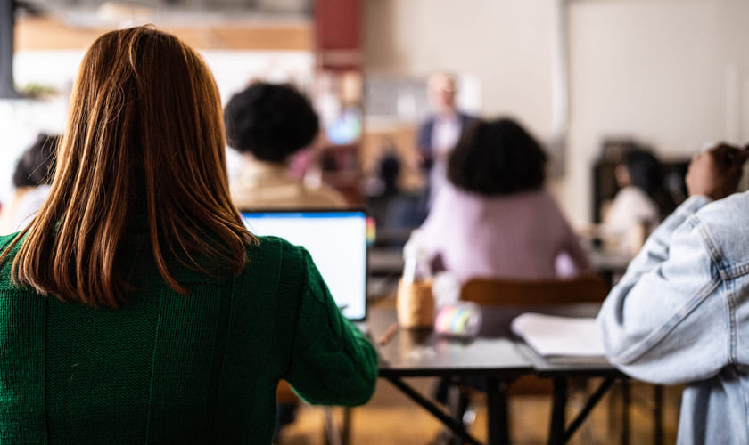 En elev sitter i et klasserom med ryggen til foran en laptop. Bilde.