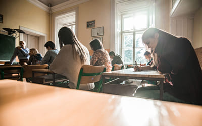 Elever sitter ved pultene sine i et klasserom og har en prøve. Bilde.