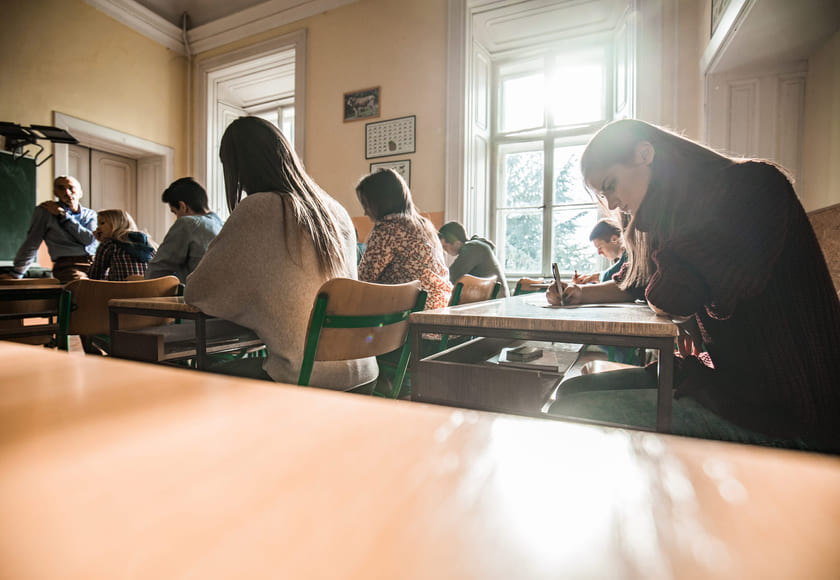 Elever sitter ved pultene sine i et klasserom og har en prøve. Bilde.