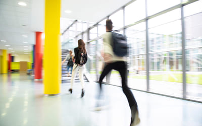 Tre elever løper gjennom en gang på en skole. Bilde.