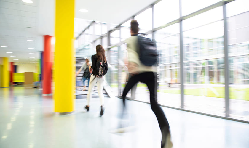 Tre elever løper gjennom en gang på en skole. Bilde.