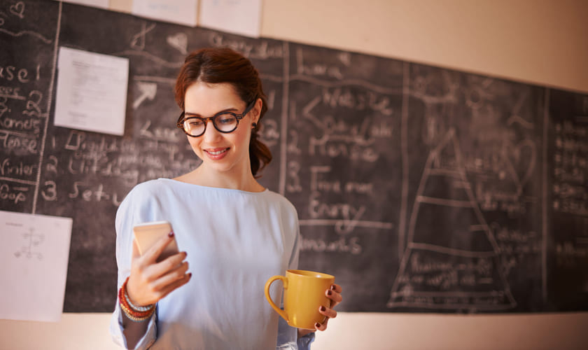 Lærer ser på mobiltelefonen foran tavla i et klasserom. Bilde.