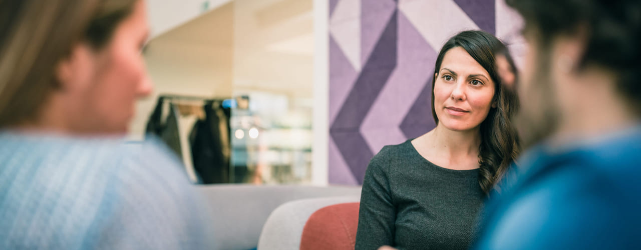 En dame sitter med to kollegaer som har ryggen til. Illustrasjonsbilde.