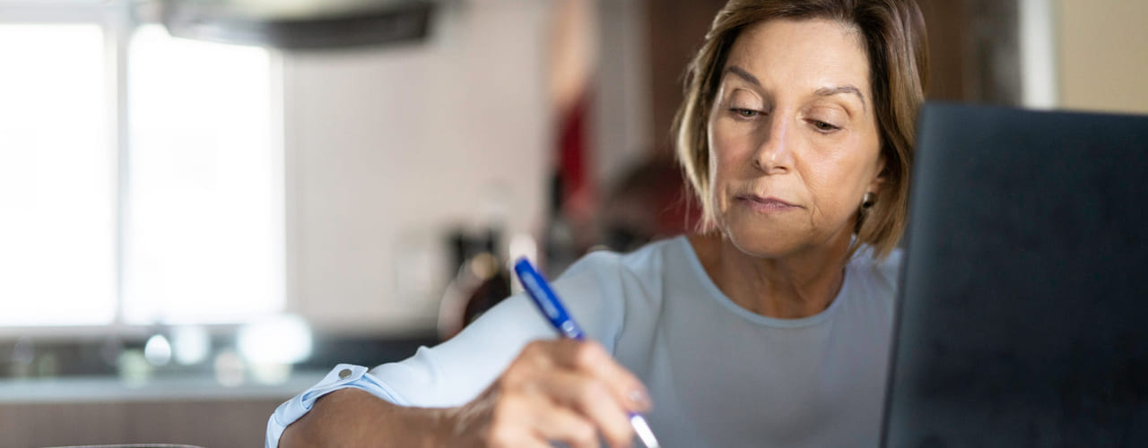 Kvinne sitter og skriver i en notatbok. Bilde.