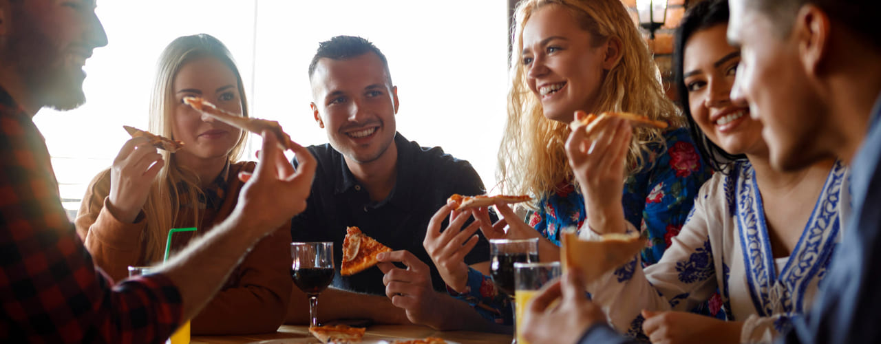 En gruppe studenter sitter rundt et bord og spiser pizza- Bilde.