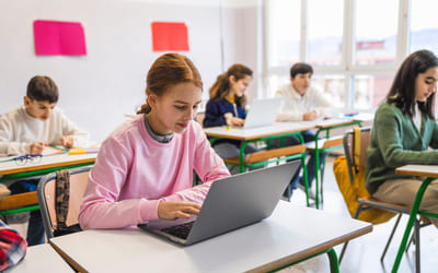 En jente sitter med en laptop i et klasserom. Illustrasjonsbilde.