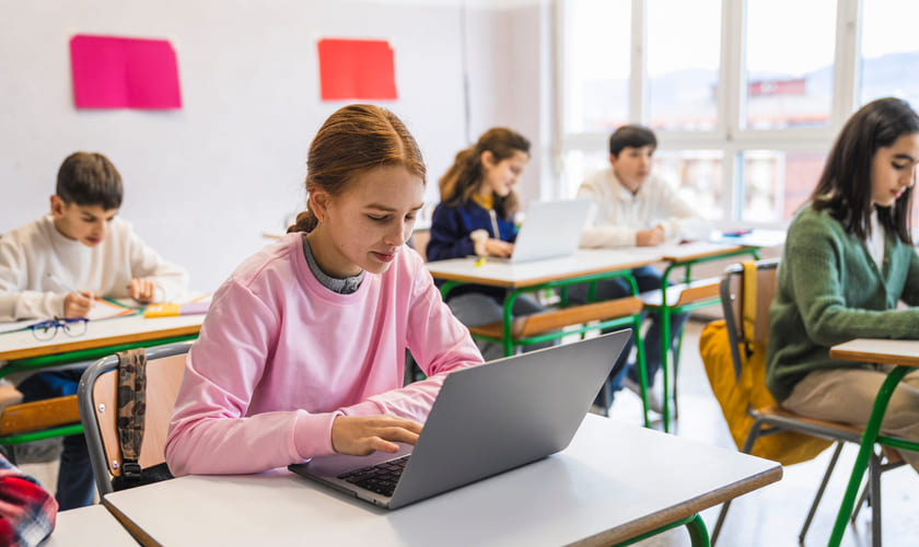 En jente sitter med en laptop i et klasserom. Illustrasjonsbilde.