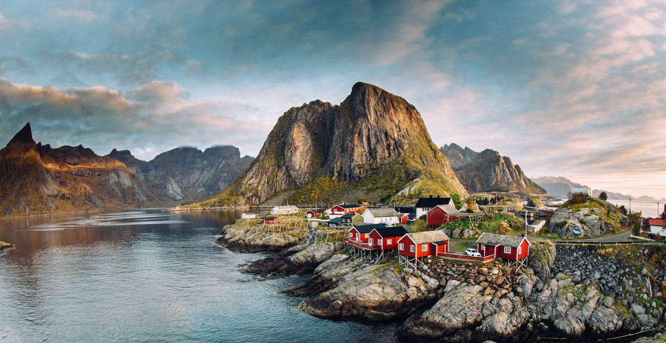 En samling av tradisjonelle hus i havgapet, fjellene troner i bakgrunnen.