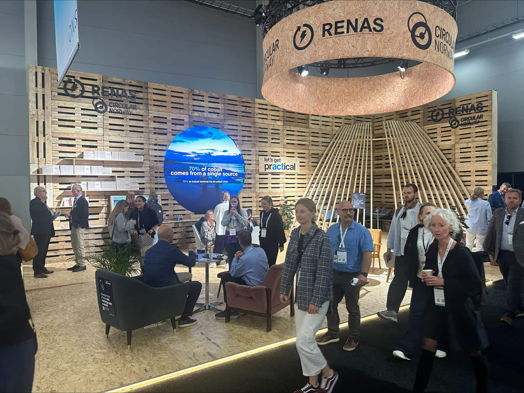 Folk som går og sitter i en messestand med en sirkulær skjerm og dekor i trepanel.