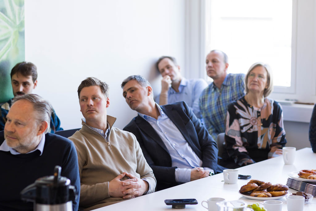 Personer samlet rundt et bord som følger med på noen som holder foredrag.