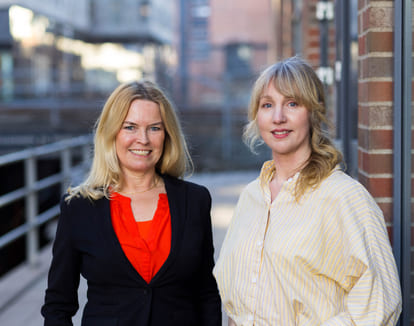 Portrett av to kvinner som står utenfor moderne blokkbebyggelse.