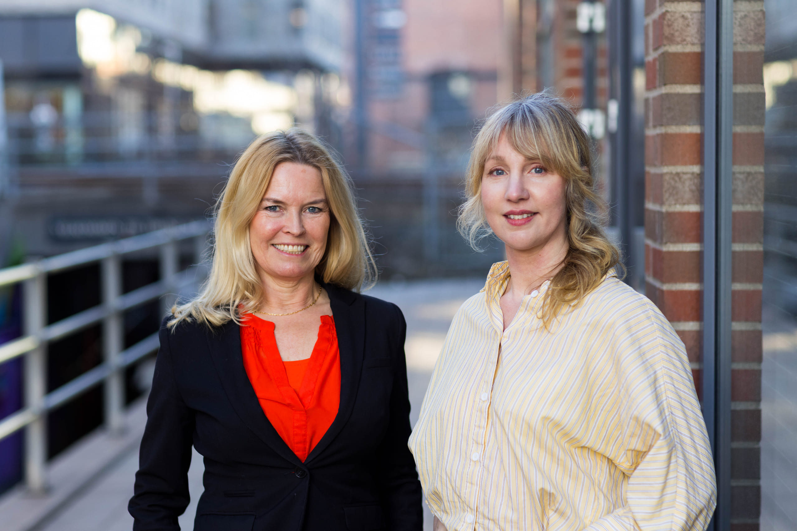 Portrett av to kvinner som står utenfor moderne blokkbebyggelse.