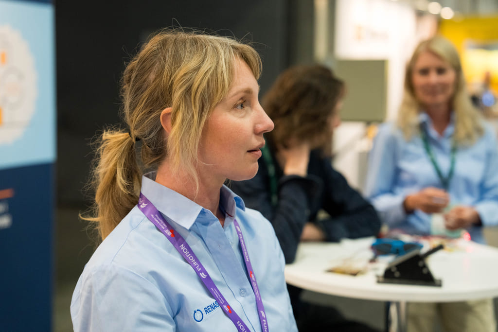 Portrett av en kvinne fra siden i blå skjorte på en stand på en messe