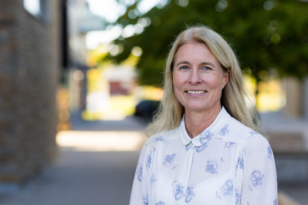 Kvinne i sommerlig skjorte står i en bygate.