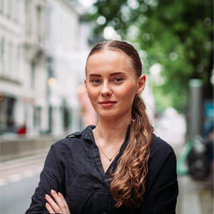 Kvinne med armene i kryss som står i en bygate.