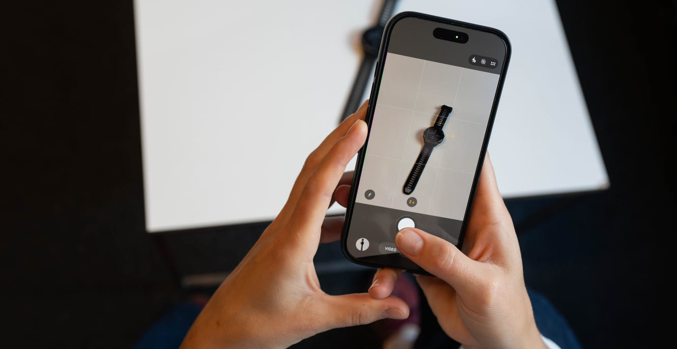 Et par hender holder i en mobiltelefon som tar bilde av en smartklokke