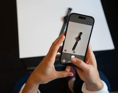 Et par hender holder i en mobiltelefon som tar bilde av en smartklokke
