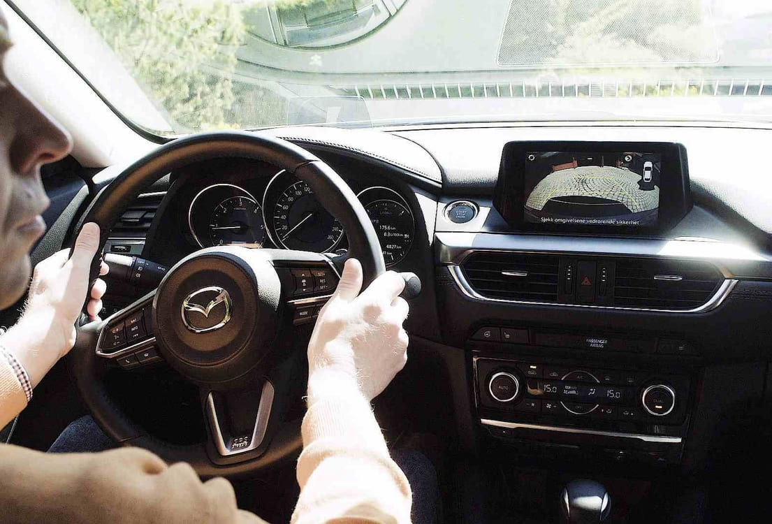 Mann inni en bil, som ser i sidespeilet når han rygger