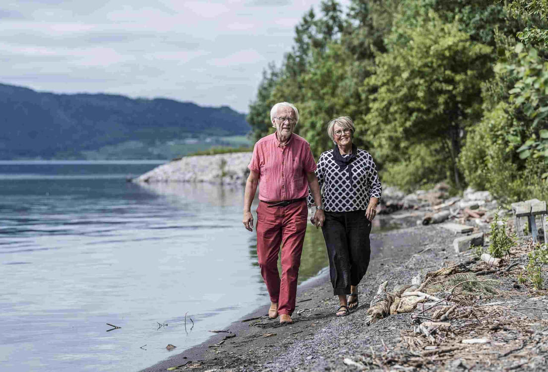Eldre par går på tur barfødt i strandkanten