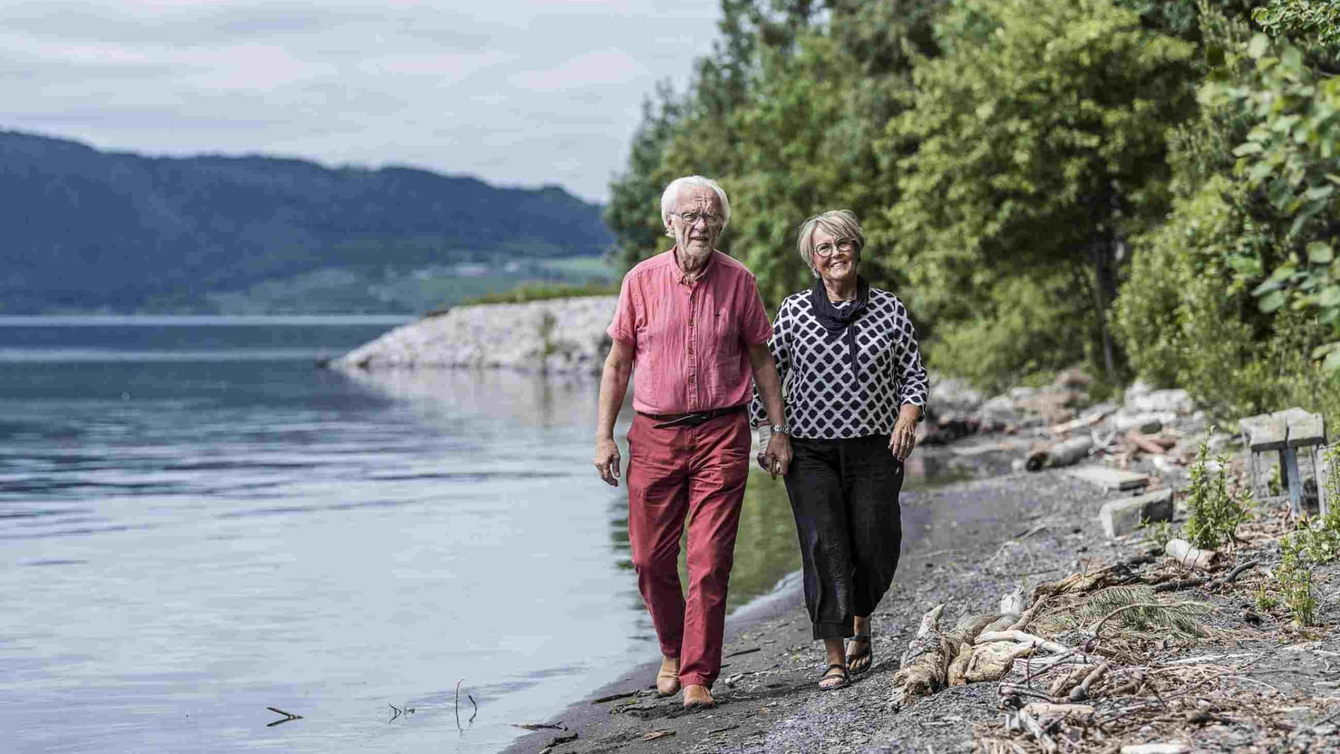 Eldre par går på tur barfødt i strandkanten