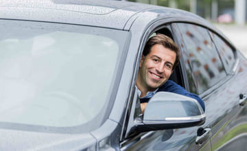 Ekspert på lån og renter, Henrik Eriksen, Santander Consumer Bank, sitter på førersiden i en bil, smiler og ser ut av vinduet