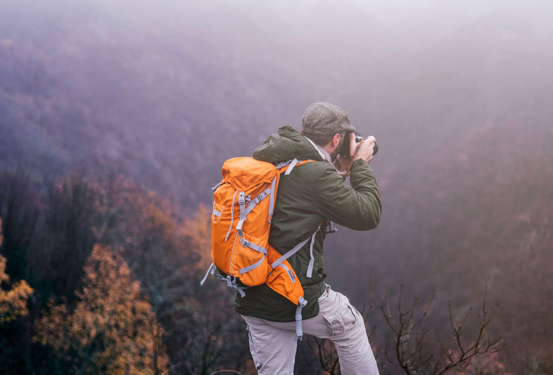 Friluftsmann med orange sekk som tar bilde utover en fjelldale