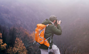 Friluftsmann med orange sekk som tar bilde utover en fjelldale