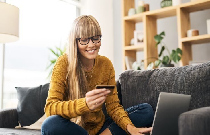 kvinne i sofa med pc og kredittkort i hånden