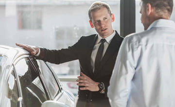 bilselger og bilkjøper i samtale ved en bil hos forhandler