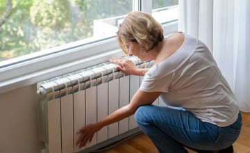 person kjenner på en varmeovn under et vindu
