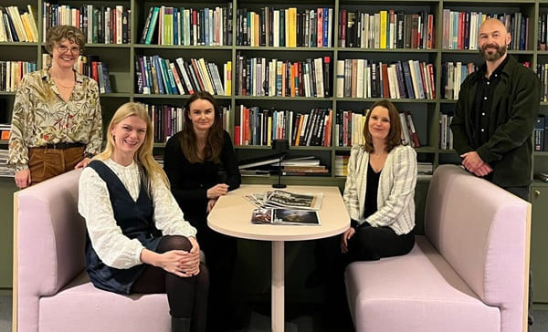 Foto av medlemmene av ekspertgruppen sittende ved et bord foran en bokhylle