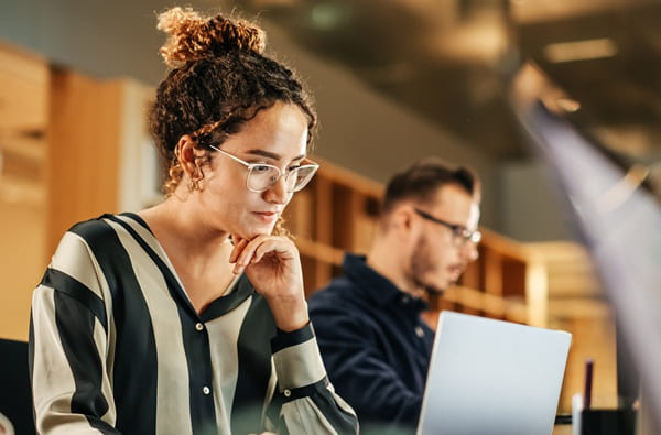 Two people working in an office, woman in the foreground, man in the background