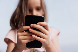 Foto av en jente som ser på moiltelefon med hender og telefon i fokus og ansiktet delvis skjult og ute av fokus