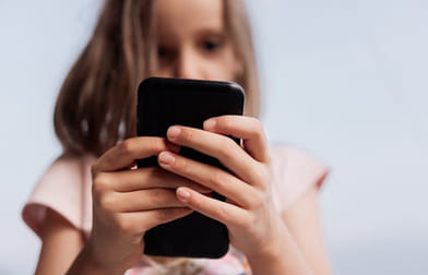 Foto av en jente som ser på moiltelefon med hender og telefon i fokus og ansiktet delvis skjult og ute av fokus